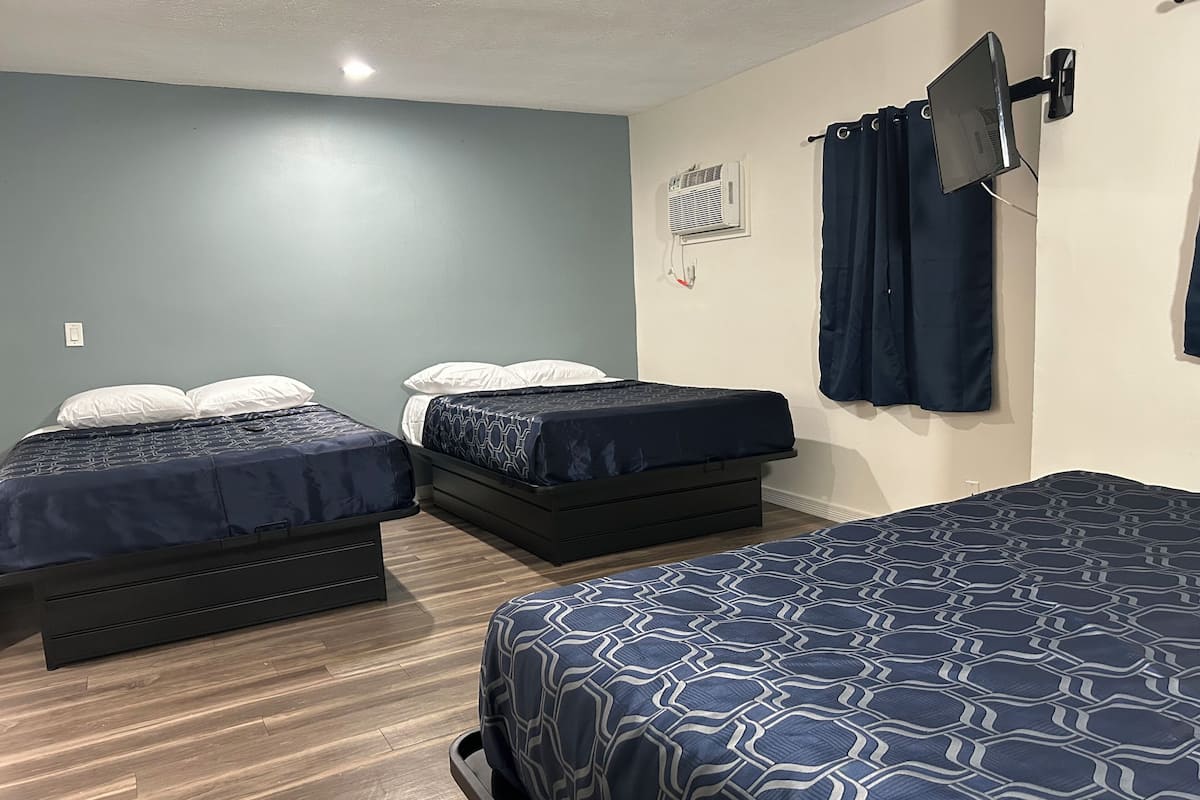 A room with two single beds, a TV mounted on the wall, and a ceiling fan.