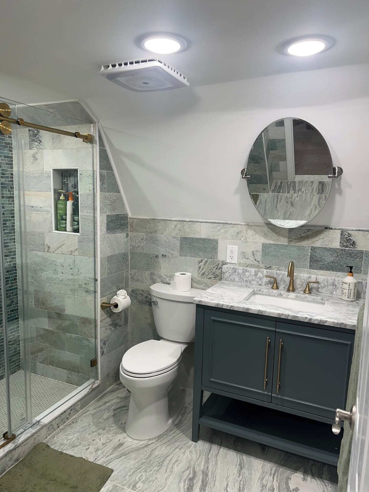 A bathroom with a shower, toilet, vanity, and a mirror.