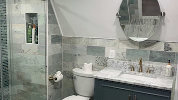 Et badeværelse med bruser, toilet, håndvask og spejl.