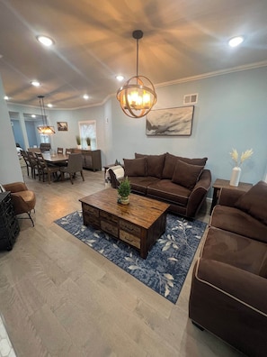A modern living room with a brown sofa, a wooden coffee table, and a dining area with chairs and a table. - Huge Family House 12 miles from NYC/4Bath/Parking (Belleville)