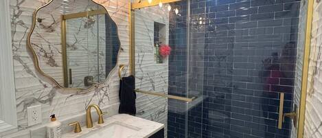Un baño con tocador de mármol, cabina de ducha de vidrio y espejo con iluminación.