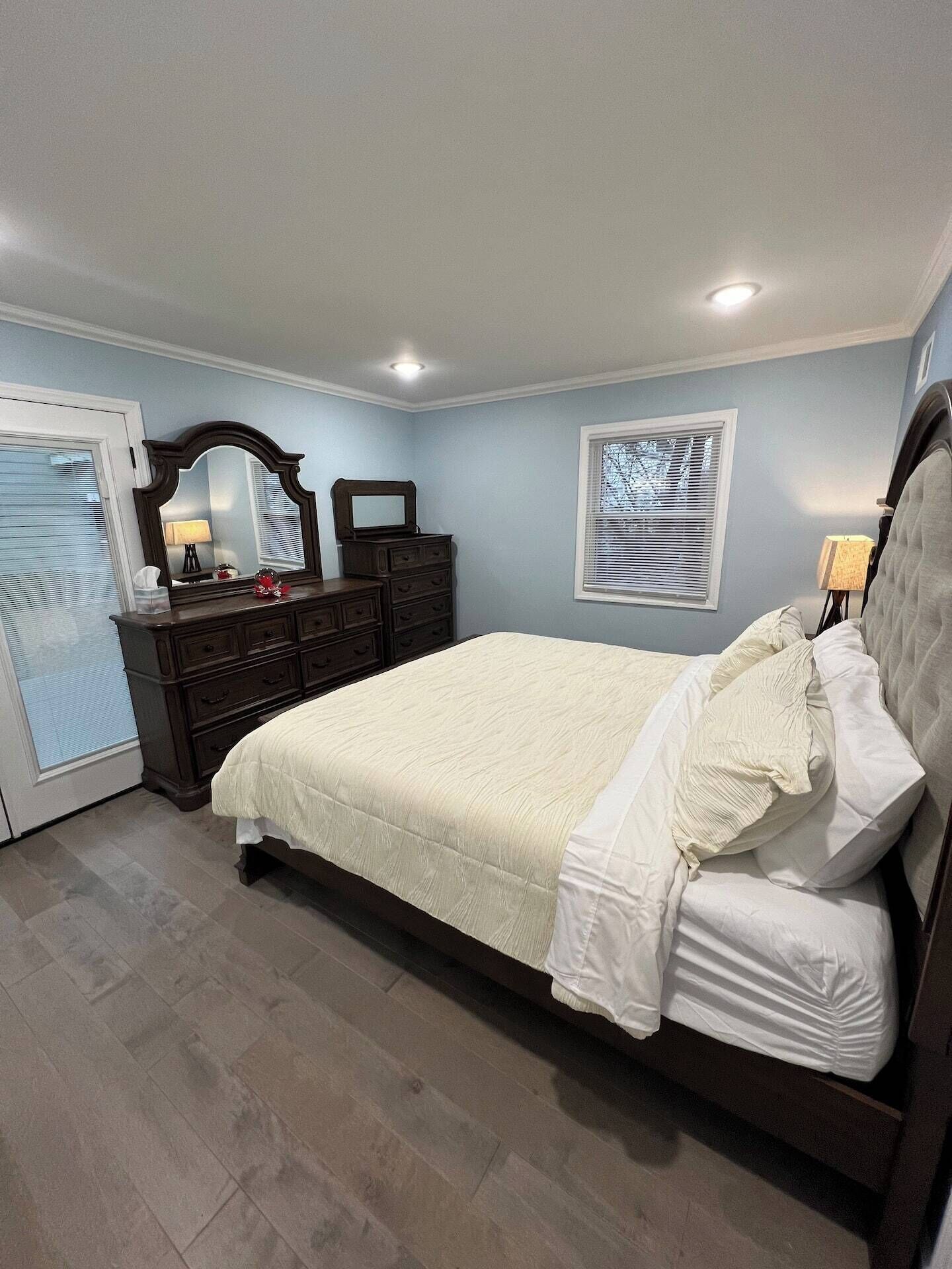 A bedroom with a bed, dresser, mirror, and window.