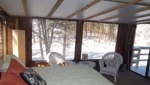 Une pièce confortable avec un lit, deux fauteuils en osier blancs, une petite table et de grandes fenêtres donnant sur un espace extérieur enneigé.