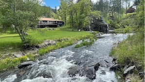 Une rivière traverse un paysage verdoyant et luxuriant, avec une maison sur la rive gauche et un affleurement rocheux au milieu.