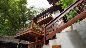 Una estructura de madera tradicional con varios niveles, incluyendo un balcón, y un cartel con texto.