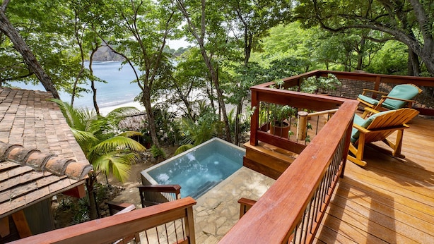 A wooden deck with a hot tub, outdoor seating, and a view of the ocean. - Beachfront 3 Bedroom Villa steps from the beach! (Tola)