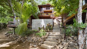 A multi-level wooden house with a stone staircase leading to the main entrance. - Beachfront 3 Bedroom Villa steps from the beach! (Tola)