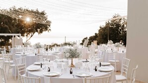 Een receptie met ronde tafels, bedekt met witte tafelkleden, witte stoelen en bloemdecoraties.
