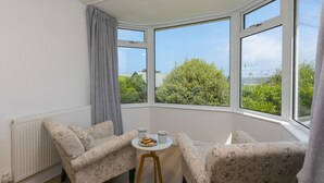 Una habitación con ventana saliente, dos sofás de estampado floral, una pequeña mesa redonda con un bol de galletas y dos tazas, y un radiador.