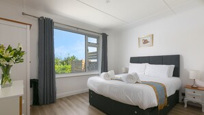 Un dormitorio moderno con una cama grande, una mesita de noche, una ventana con cortinas y vistas a zonas verdes.