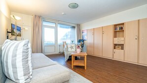 Ein modernes Wohnzimmer mit einer Couch, einem kleinen Tisch und Blick auf die Stadt durch große Fenster.