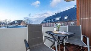 Ein Balkon mit Tisch, Stühlen, einer Flasche und einer Blume.