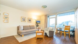 Ein Wohnzimmer mit einer Couch, einem kleinen Tisch, einem Sessel und Blick durch große Fenster.