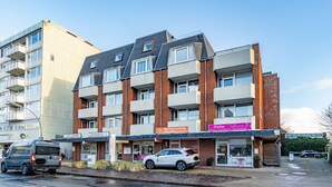 Ein mehrgeschossiges Gebäude mit einer Mischung aus Gewerbe- und Wohneinheiten. Es sind Schilder für ein Restaurant, einen Friseursalon und ein Möbelgeschäft zu sehen.