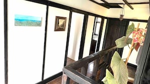 A room with a balcony, a wooden floor, a black railing, and a potted plant.