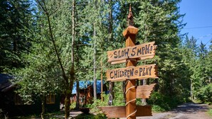 A wooden signpost with 'SLOW 5 MPH' and 'CHILDREN @ PLAY' signs in a forested area. - Cozy retreat, newly renovated with loft, hot tub, creek access, pet friendly (Rhododendron)