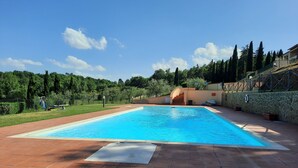 Ein rechteckiger Swimmingpool mit einer gefliesten Terrasse, umgeben von einer Steinmauer und Grünpflanzen.
