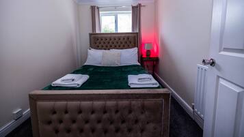 A neatly made bed with a tufted headboard, a bedside table with a lamp, and a window with curtains.