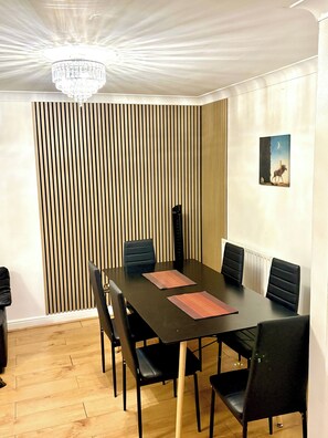 Un espace repas comprenant une table, des chaises, un lustre, un tableau accroché au mur et un mur avec des lambris verticaux.