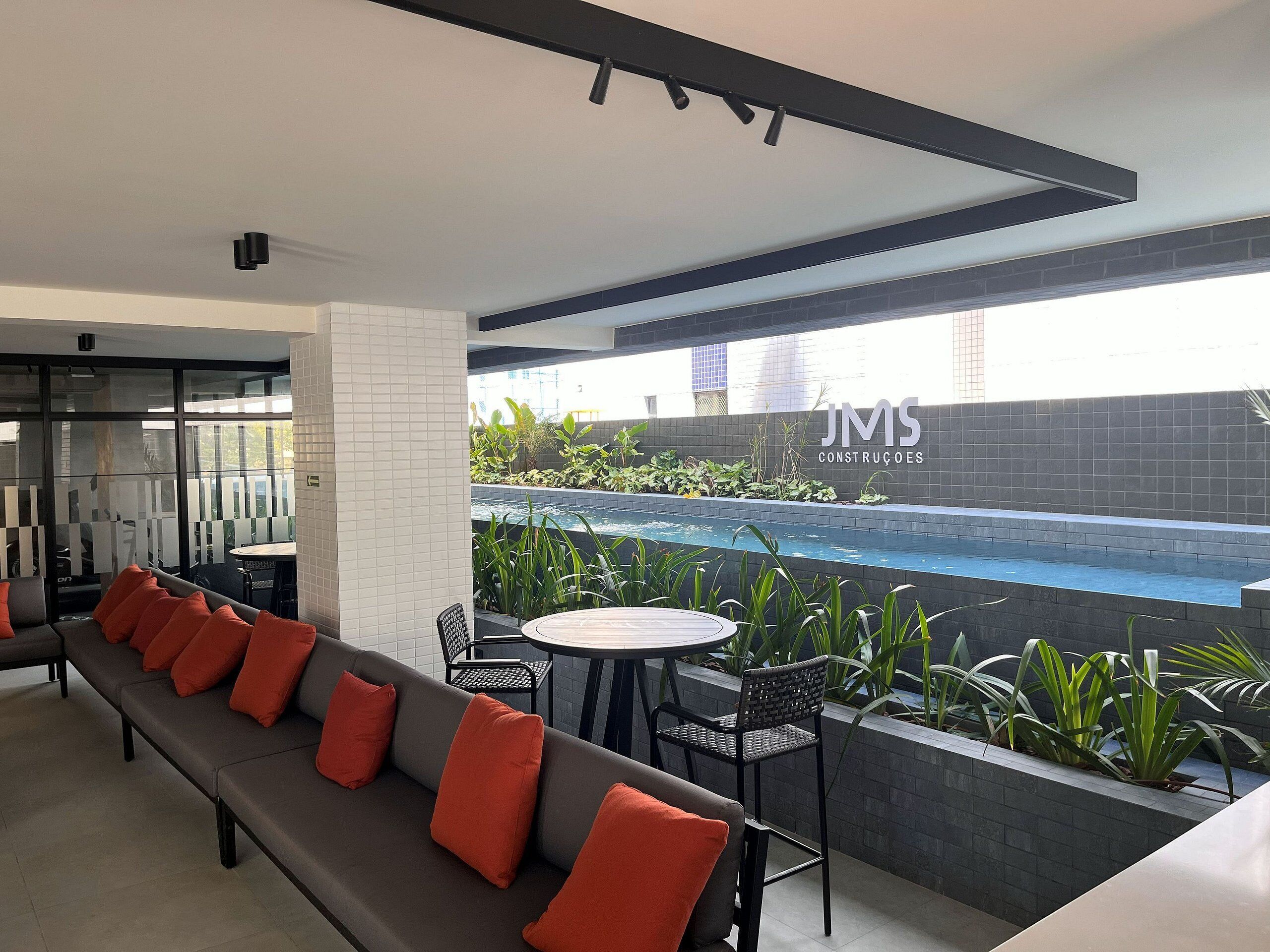 Un espace extérieur moderne avec des sièges, une piscine, une enseigne indiquant « JMS Construcções » et une vue sur le paysage urbain.