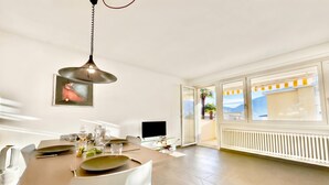 A dining area with a table set for two, a hanging light fixture, a flat-screen TV, and a view of the outdoors.