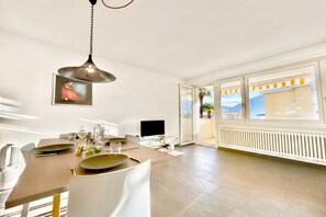 A dining area with a table set for two, a hanging light fixture, a flat-screen TV, and a view of the outdoors. - Malibu46, Minusio, Switzerland (Minusio)