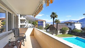A balcony with a pool, a dining table, chairs, and a view of a mountain.