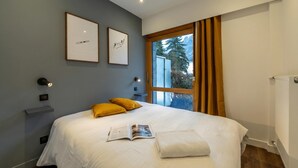 A bedroom with a bed, a window with curtains, a wall-mounted light, and a framed picture. - Sweet Home Brevent 2-Min Ski Lift + Private Garden, Chamonix, France (Chamonix)
