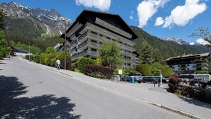A multi-story building with balconies, a parking area, and a mountainous backdrop. - Sweet Home Brevent 2-Min Ski Lift + Private Garden, Chamonix, France (Chamonix)