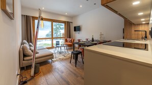 A modern kitchen with a built-in island, a dining area with a table and chairs, a sofa, and a large window with curtains. - Sweet Home Brevent 2-Min Ski Lift + Private Garden, Chamonix, France (Chamonix)