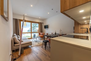 A modern kitchen with a built-in island, a dining area with a table and chairs, a sofa, and a large window with curtains.