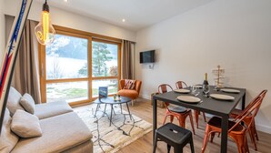 A modern living room with a sofa, a dining table set for four, and a large window with a view of a snowy landscape. - Sweet Home Brevent 2-Min Ski Lift + Private Garden, Chamonix, France (Chamonix)
