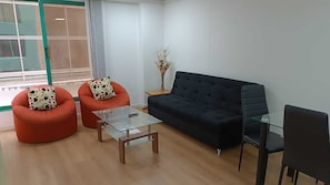 A modern living room with a dark blue sofa, two orange armchairs, a glass coffee table, and a glass dining table with chairs. - Acogedora suite La Carolina sobre la Republica del Salvador, con piscina. (Quito)