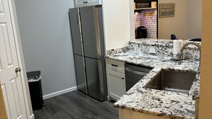 Eine kompakte Küche mit einem Edelstahlkühlschrank, einem eingebauten Geschirrspüler und einer Arbeitsplatte aus Granit.