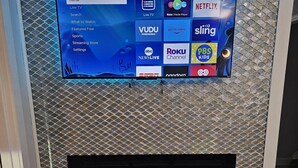 Ein TCL Roku Fernseher an einer strukturierten Wand, darunter ein Kamin.