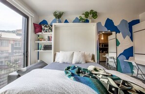 Ein modernes Schlafzimmer mit einem Bett, einem Nachttisch, einem Regal mit Büchern, einem Fenster und Ausblick nach draußen.