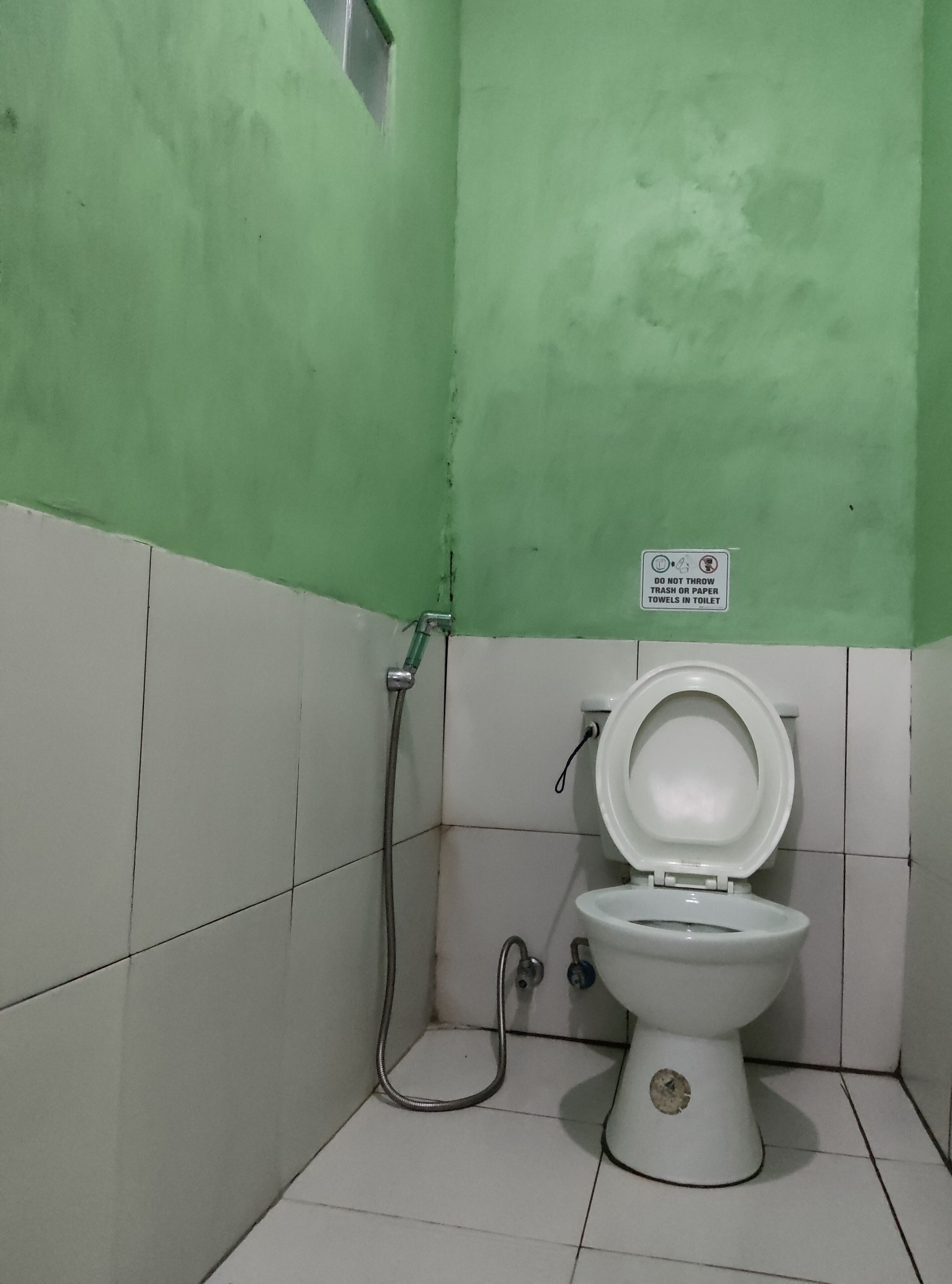 A small, basic bathroom with a toilet, a shower, and a sign instructing not to throw trash or paper towels in the toilet.