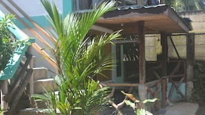 A wooden structure with a tiled roof, surrounded by plants and a stone wall. - Shenamae Pension  (San Vicente)