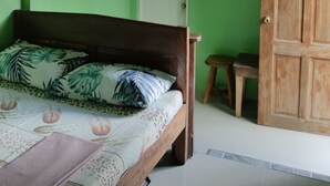 A bedroom with a bed, a wooden door, and a small stool. - Shenamae Pension  (San Vicente)