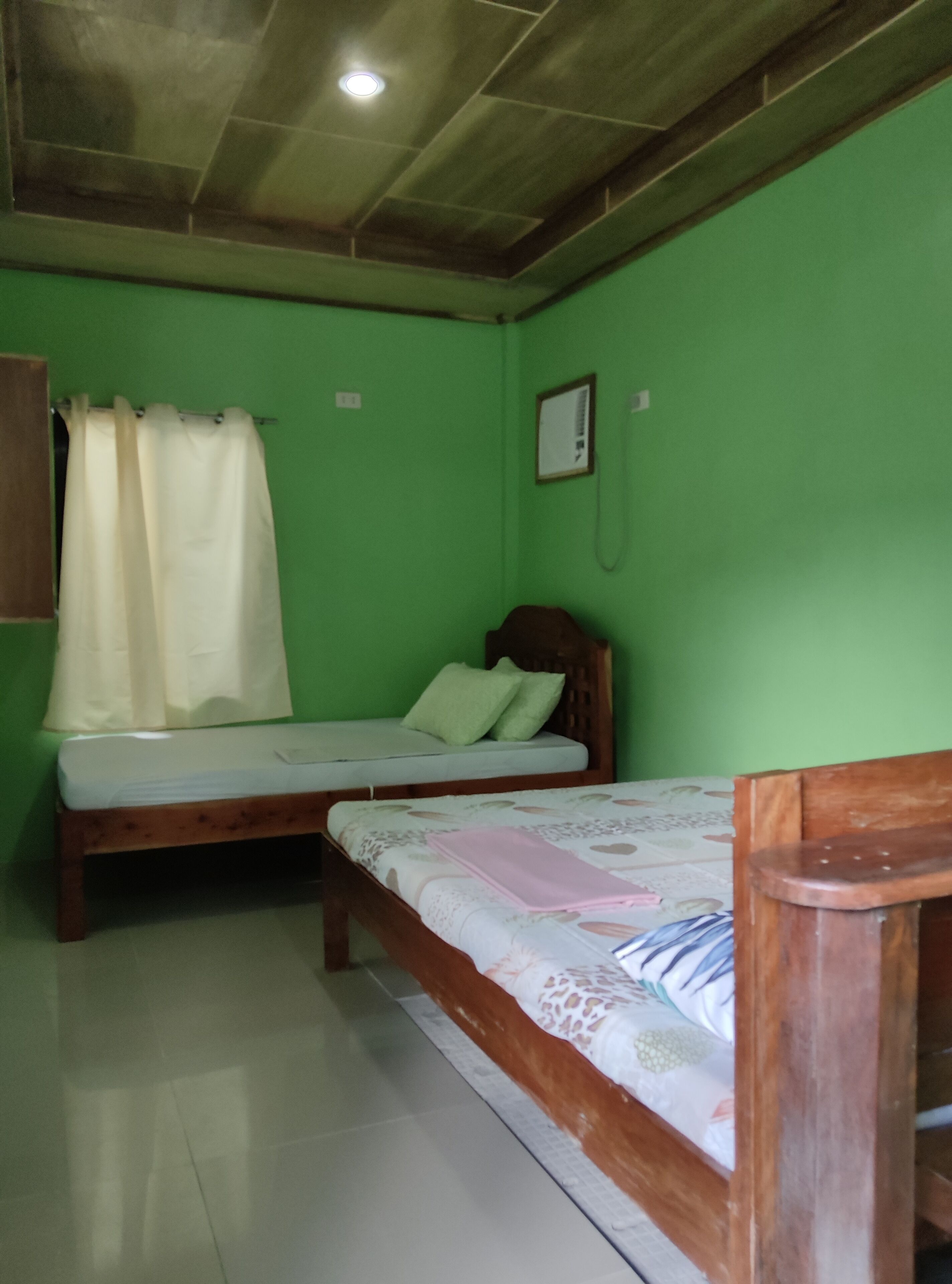 A room with two wooden beds, green walls, a white curtain, and a wooden headboard.