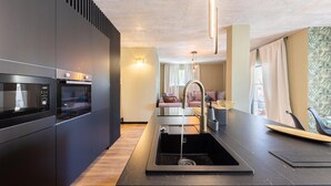 A modern kitchen with built-in appliances, a central island with a sink, and a view of a living area with a sofa and a window.