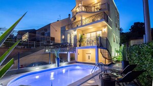 A multi-story building with a swimming pool, outdoor seating, and a staircase leading to the upper floors.