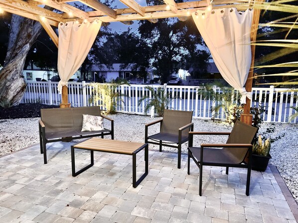 An outdoor patio with four chairs and a table, surrounded by a white picket fence and trees. - The Mango House Cozy Beach Cottage (Sarasota)