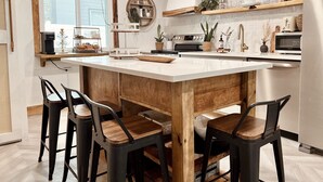 Una cocina moderna con una isla central, sillas de madera, una cafetera y diversos electrodomésticos.
