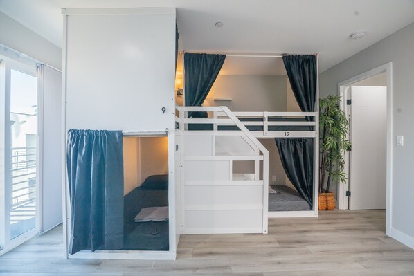 A room with a bunk bed, a sliding door, a potted plant, and a view of the outside. - Normandie Hostel (Los Angeles)