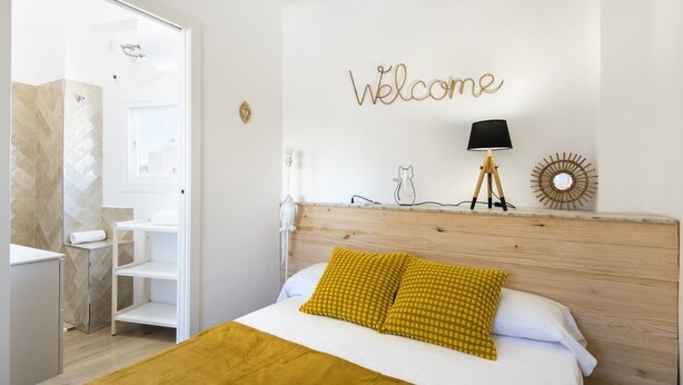 A hotel room with a bed, a wooden headboard, a 'Welcome' sign, a lamp, and a wall decoration. - Apartment Málaga tour Museums Constitucion Square (MALAGA)
