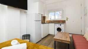 A compact room with a bed, a small table, a sofa, a washing machine, a refrigerator, and a TV mounted on the wall. - Apartment Málaga tour Museums Constitucion Square (MALAGA)