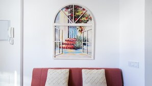 A red sofa with two patterned cushions, a white wall, and a window with a painting of a colorful outdoor scene. - Apartment Málaga tour Museums Constitucion Square (MALAGA)