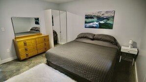 Une chambre à coucher comprenant un lit, une commode, une armoire, une table de chevet et un tableau accroché au mur.