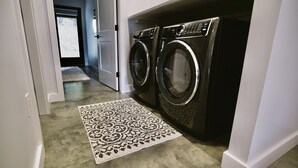 Une buanderie équipée de deux lave-linge et deux sèche-linge à chargement frontal, d’un tapis à motifs et d’une porte donnant sur un couloir.